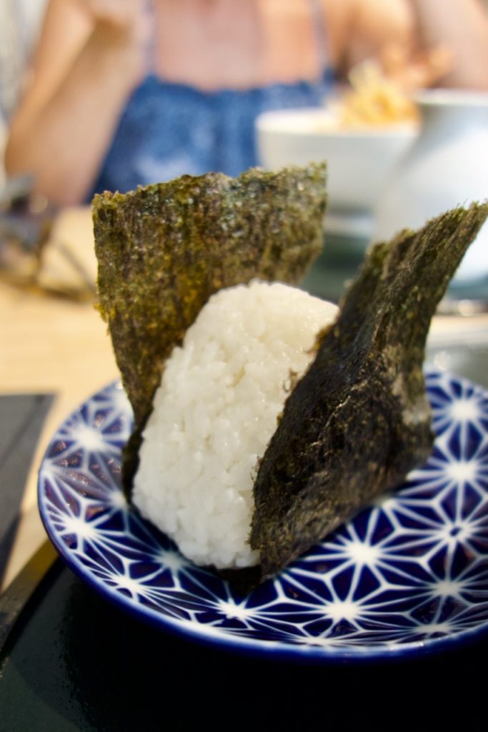 Onigiri entourée d'une feuille d'algue nori dans une assiette bleue et blanche