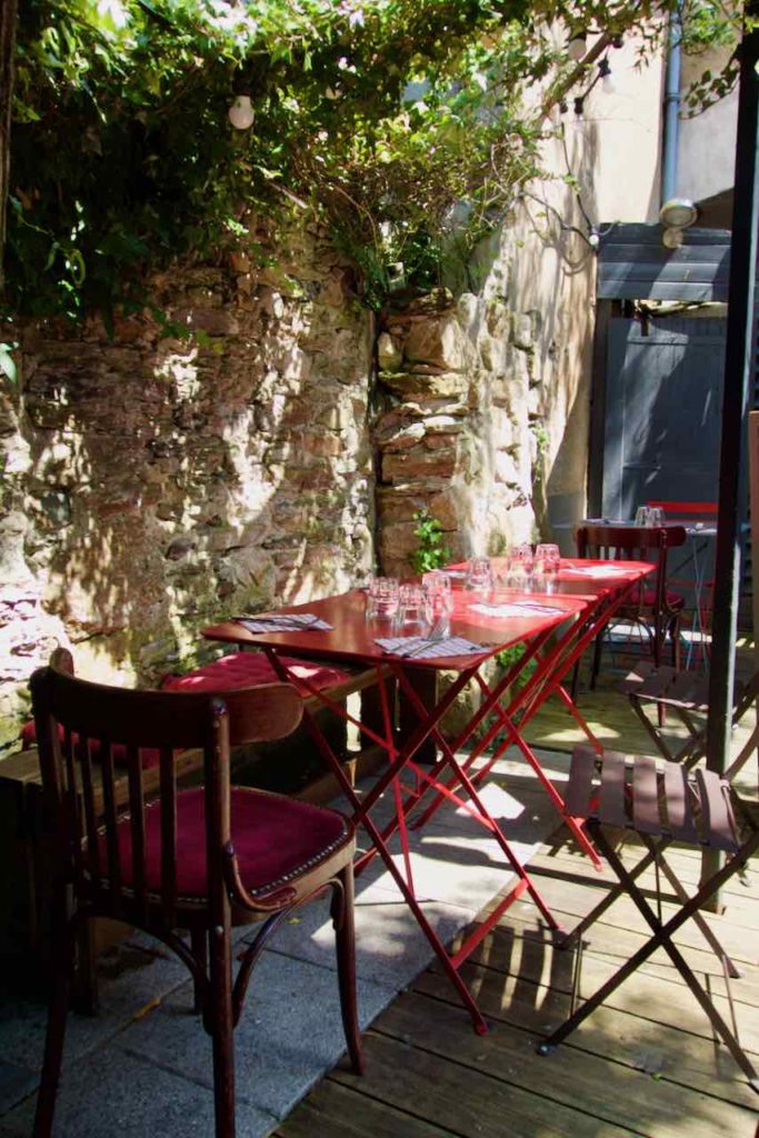 Patio avec tables et chaises rouges, sol en bois, mur en pierre et guirlande guinguette 