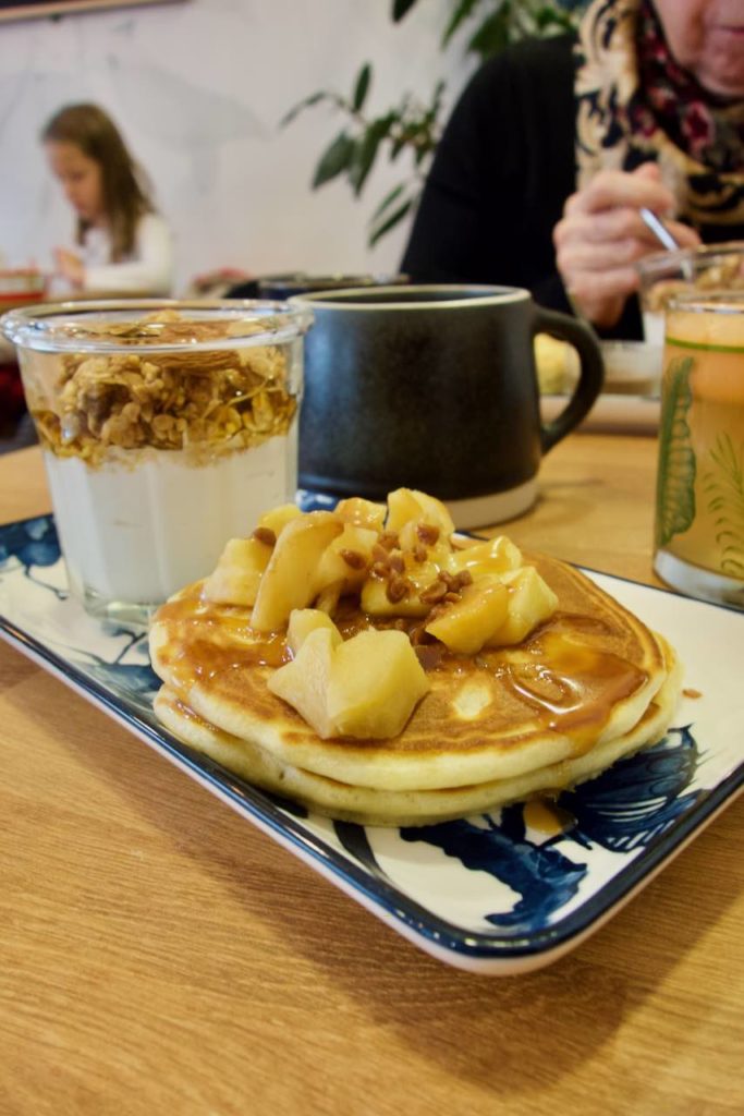 Pancakes aux pommes au premier plan, fromage blanc et granola au second blanc dans une assiette rectangulaire bleue et blanche