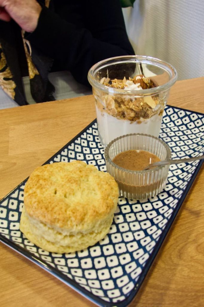 Scone, pâte à tartiner dans un petit récipient en verre, granola au second plan dans une assiette bleue et blanche