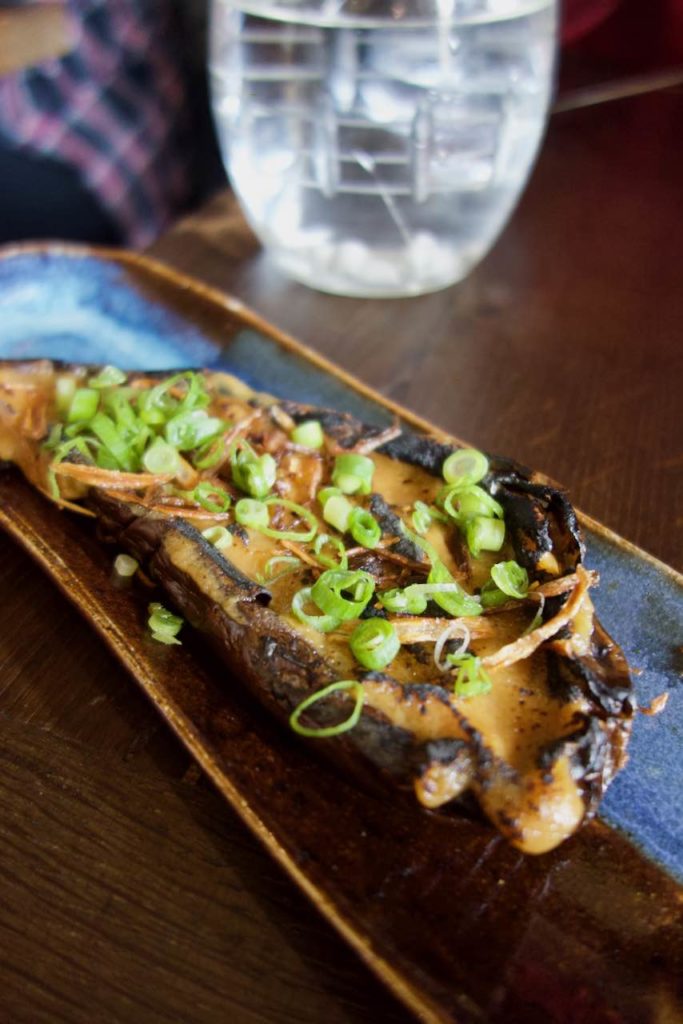 Aubergine au miso surmontée de cébette dans une assiette en terre bleue