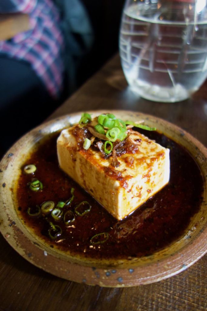Tofu soyeux et sa réduction de sauce soja surmonté de cébette dans une assiette de type grès