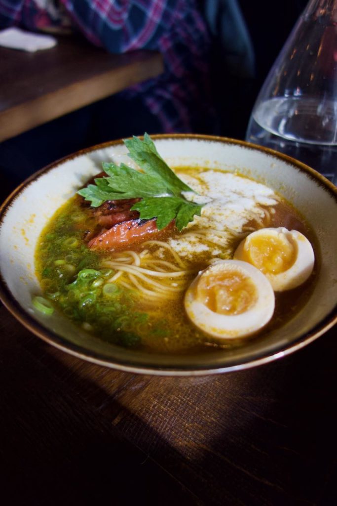 bol de ramen avec des cébettes, un oeuf mollet mariné, une tomate braisée, une feuille de shiso et de la mozzarella