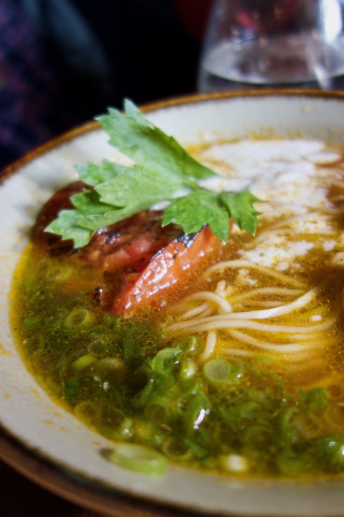 vue rapproché d'un bol de ramen avec de la cébette, une tomate braisée et une feuille de shiso