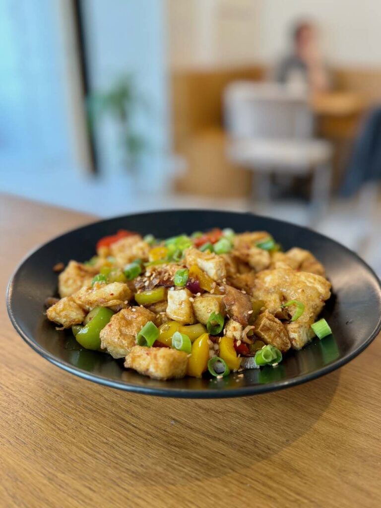 Tofu frit, poivrons, oignons et shiitake dans une assiette creuse noire