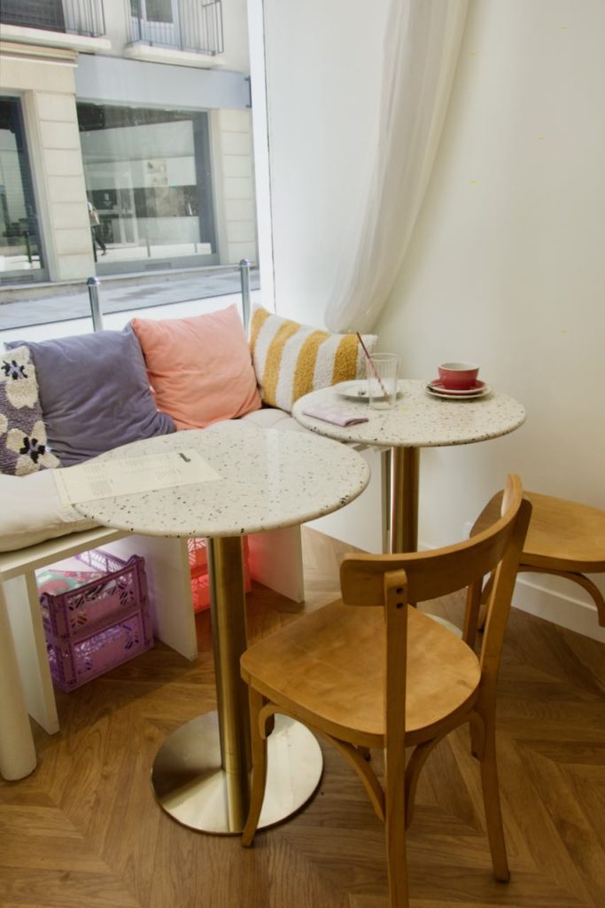 Tables en bois, chaises bistro blanc à points noirs, banquette et coussins pastel