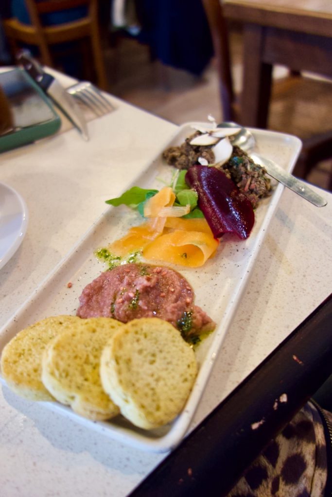 Croûtons, houmous de betterave, tapenade de champignon dans une assiette blanche allongée