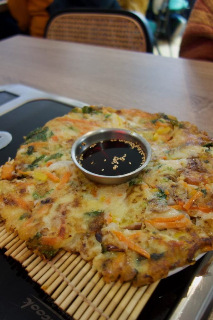 Galette de légume avec une coupelle de sauce soja au milieu et servie sur une paillasses en bambou