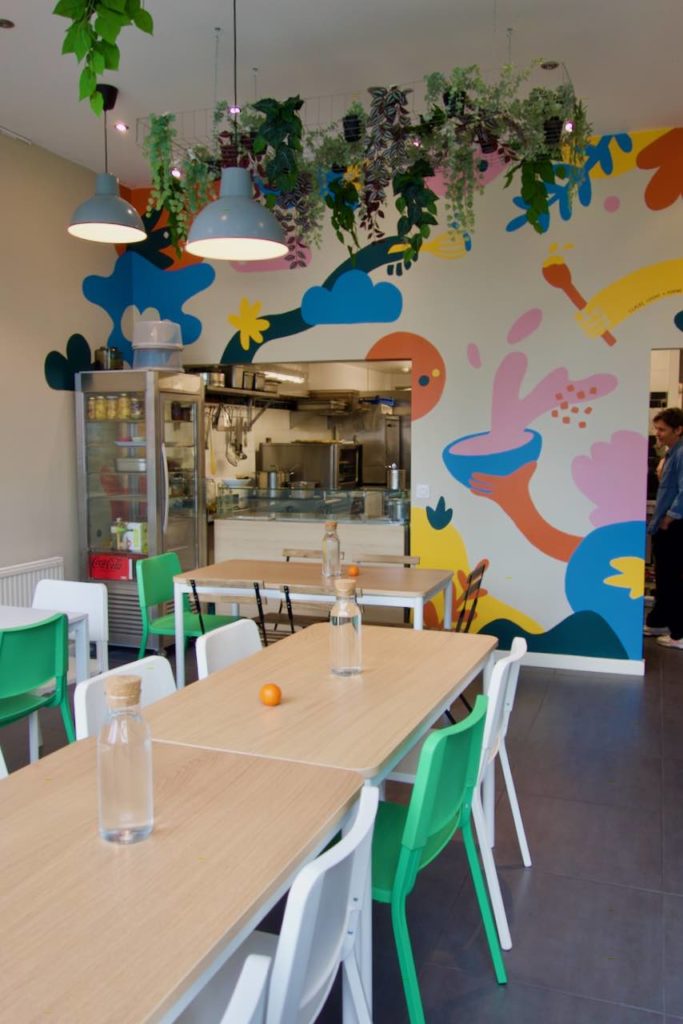 Intérieur de la cantine avec des tables en bois et une grande fresque colorée au mur