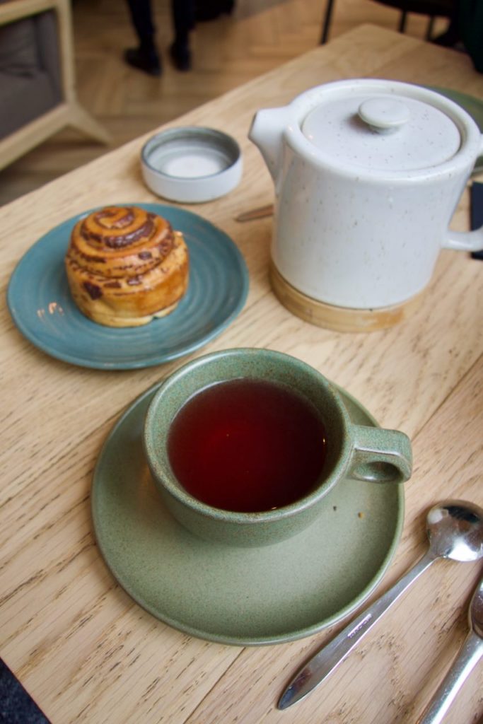 Infusion dans une tasse verte, roulé sur une assiette bleue et théière blanche sur une table en bois