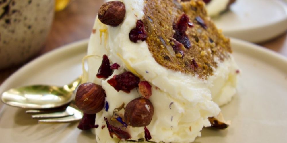 Carrot cake avec un glaçage surmonté de noisettes dans une assiette blanche