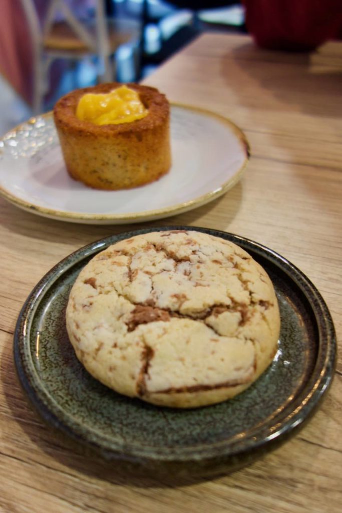 Cookie dans une assiette noir au premier plan et moelleux aux fruits exotiques dans une assiette blanche en arrière plan
