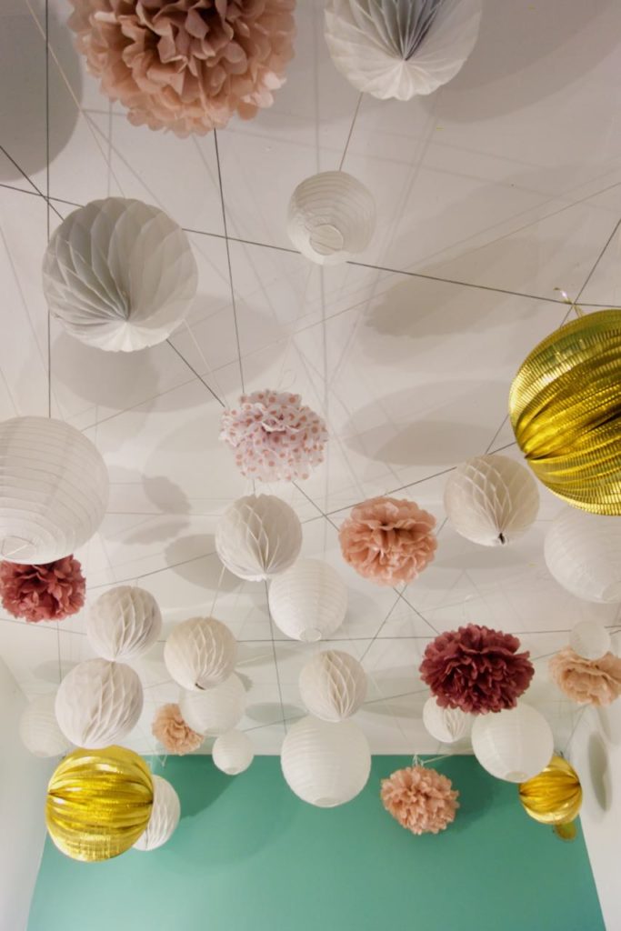 Plafond parsemé de boules géométriques en papier blanches et de couleurs roses ou dorées