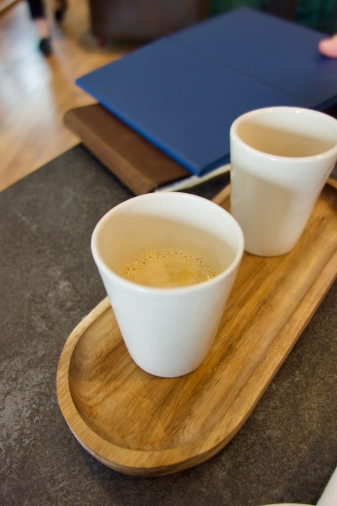 Deux verres blanc contenant un bouillon jaune sur une tablette en bois