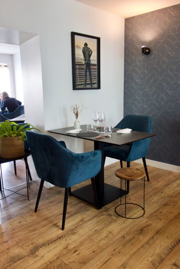 Intérieur du restaurant avec chaises en velours bleu, table noir, parquet et murs blancs et gris foncé