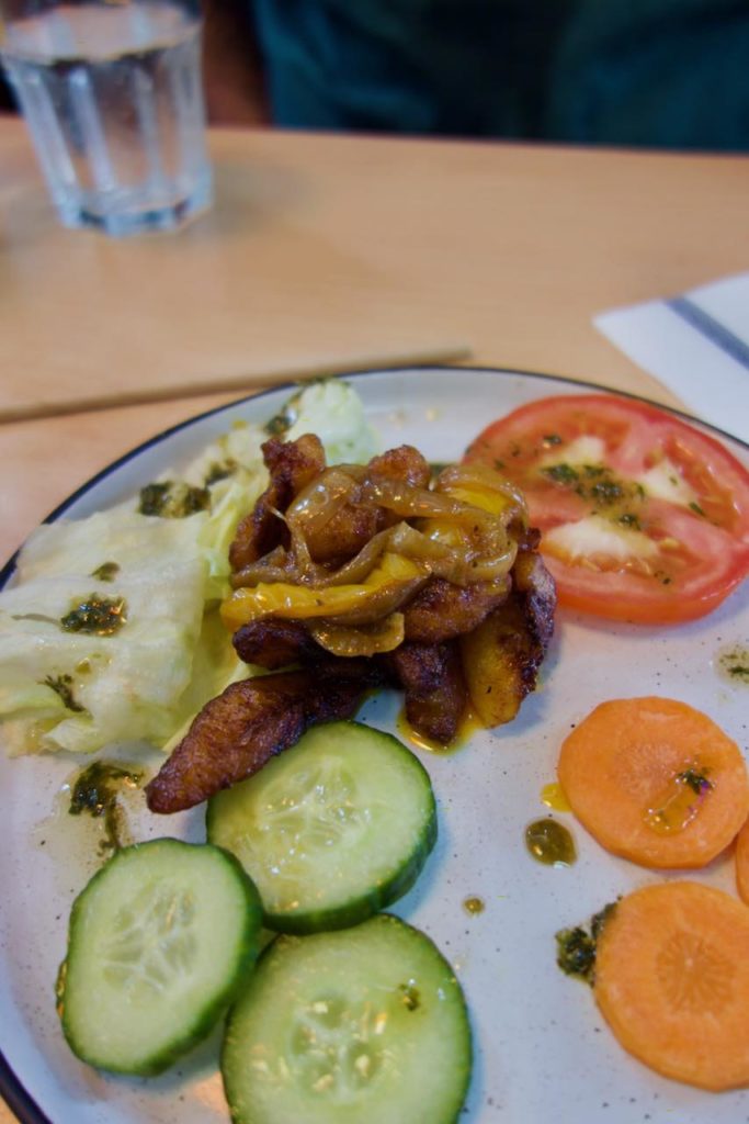 Alloco, concombre, carottes crus, salade et tomate dans une assiette blanche