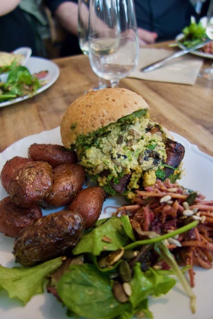Burger, pommes de terre, salade et coleslaw dans une assiette blanche sur une table en bois