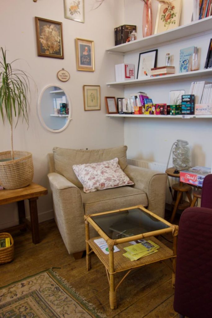 Un large fauteuil beige, une table en bambou, des étagères blanches avec des livres au mur