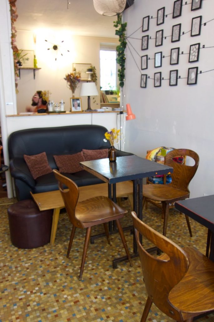 Salle du restaurant avec tables et chaises en bois foncé, carrelage à petits carreaux, canapé noir et cadres au mur