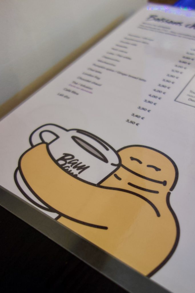 Menu de Bambam Café avec la mascotte jaune qui sert un mug dans ses bras