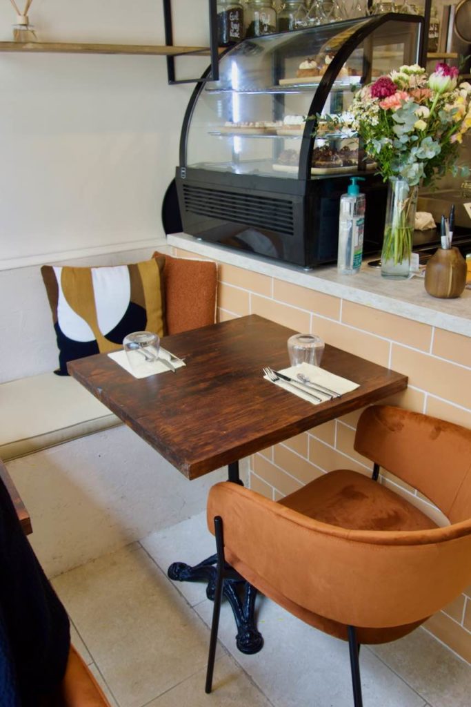 Intérieur du restaurant avec une table de bistro en bois, un fauteuil velours terracota et une banquette avec des coussins