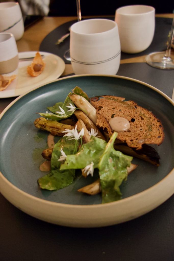 Asperges blanches, tuile olive et émulsion dans une assiette grise à bords hauts