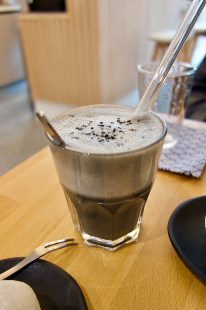 Latté au sésame noir servi dans un verre transparent avec une paille en verre. Belle couche de mousse et graines de sésame noir sur le dessus