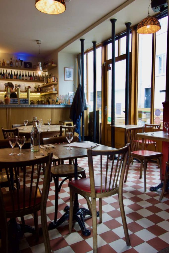 Intérieur du Brocéliande, parterre à carreaux, tables et chaises bistro en bois, zinc jaune en fond et larges baies vitrées