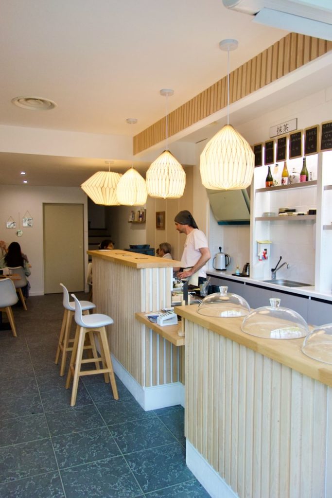 Intérieur avec un bar en bois, deux tabourets hauts, des luminaires en bois clair