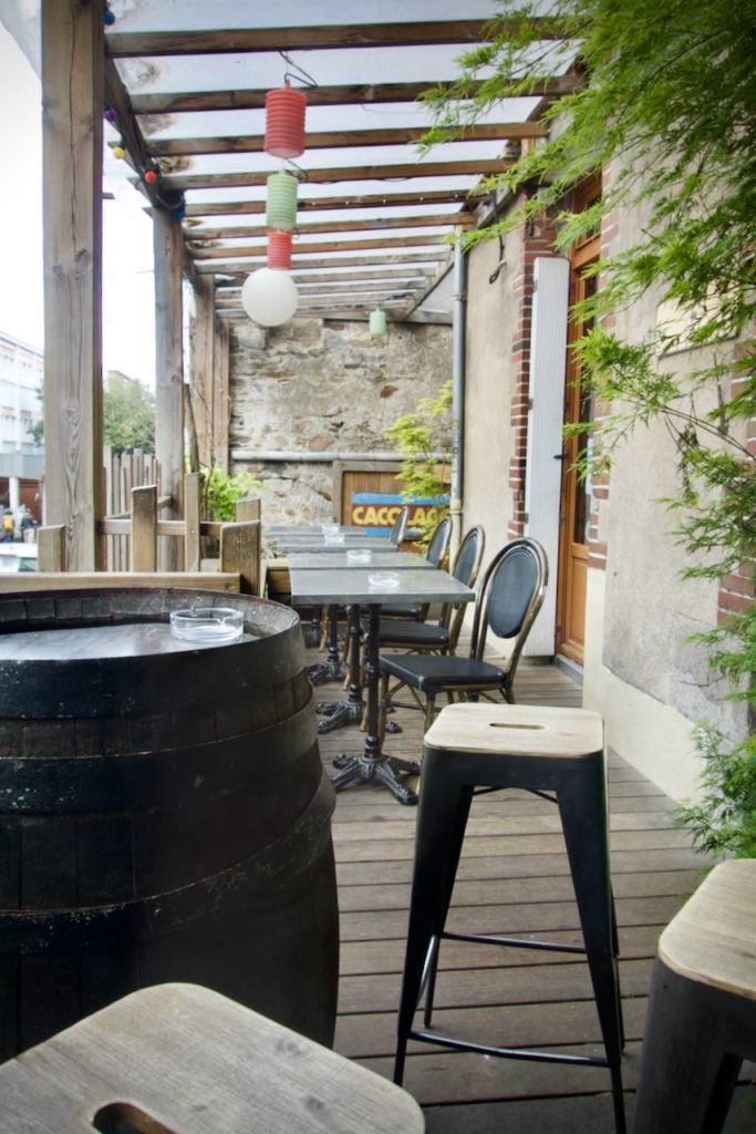 Loggia avec sol parquet, tables et chaises bistro grises, fût et tabourets hauts