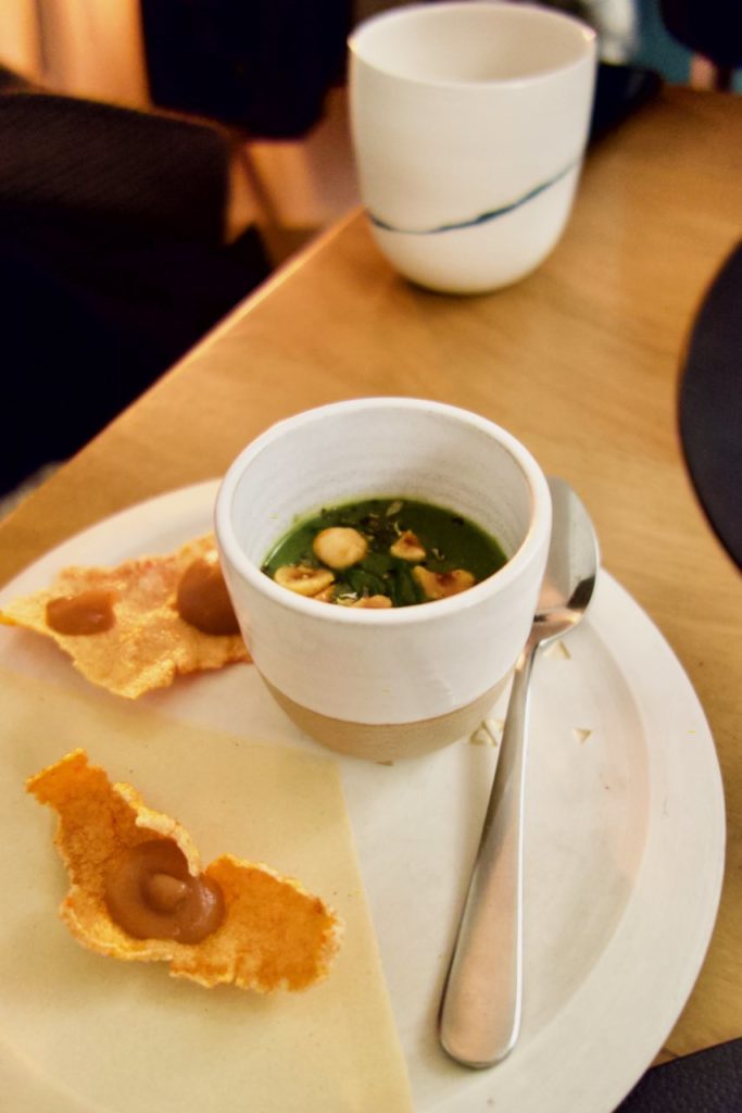 Velouté d'orties dans un ramequin blanc accompagné de tuiles au paprika dans une assiette blanche et jaune