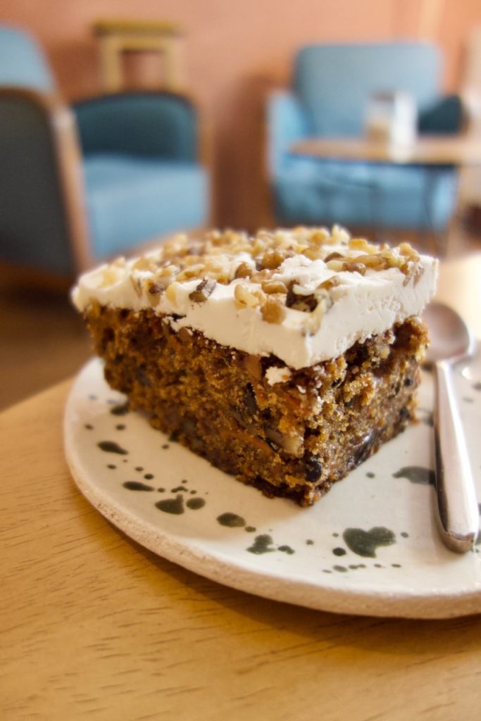 Carrot cake avec un glaçage blanc épais surmonté de noisettes dans une assiette en grès blanc mouchetée vert