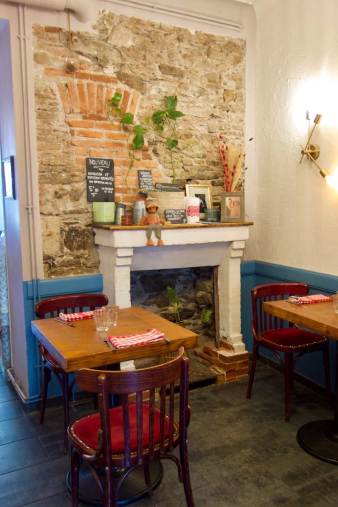 Cheminée comblée blanche, mur en pierres de taille, tables et chaises bristrot en bois