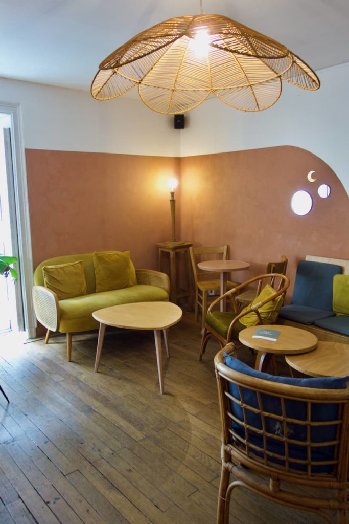 Salon cosy avec canapé velours vert, petites tables en bois design, fauteuils en rotin avec coussin, parquet et luminaire en bois, mur terracotta
