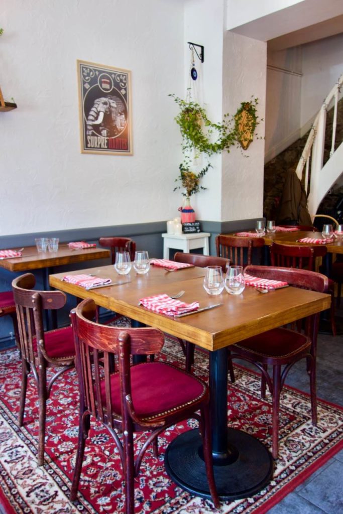 Table bistro en bois, chaise bistro bois et velours rouge, tapis rouge au sol, mur sblancs