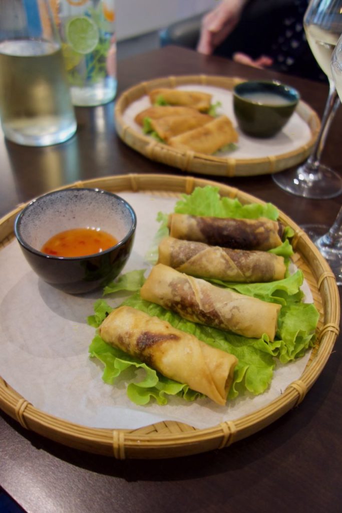 Quatre nems sur de la laitue accompagnés d'une sauce sucrée dans un plat tressé en bambou