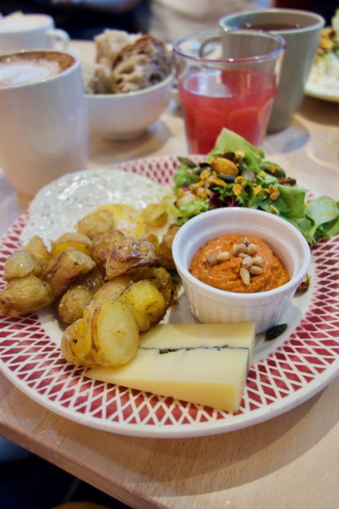 Pommes de terre rissolées, tapenade de poivrons dans un ramequin blanc, salade, oeuf au plat et fromage dans une assiette blanche et rouge