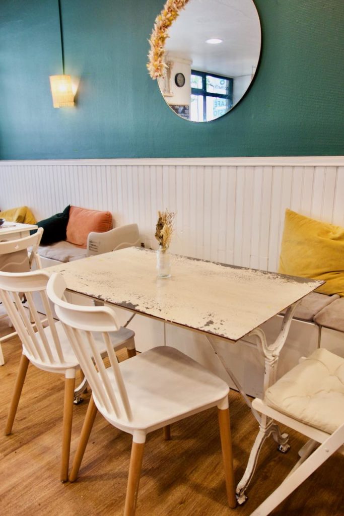 Table vintage en fer blanc, chaises en bois et banquette avec des oreillers en velours, miroir au mur