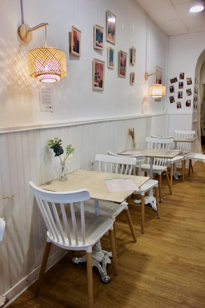 Tables en fer blanc vintage, chaises en bois blanc, parquet, cadres au mur, luminaires en bambou