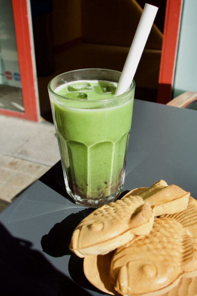 Bubble tea au matcha et azuki dans un verre transparent, deux taiyaki au premier plan dans une assiette en bambou