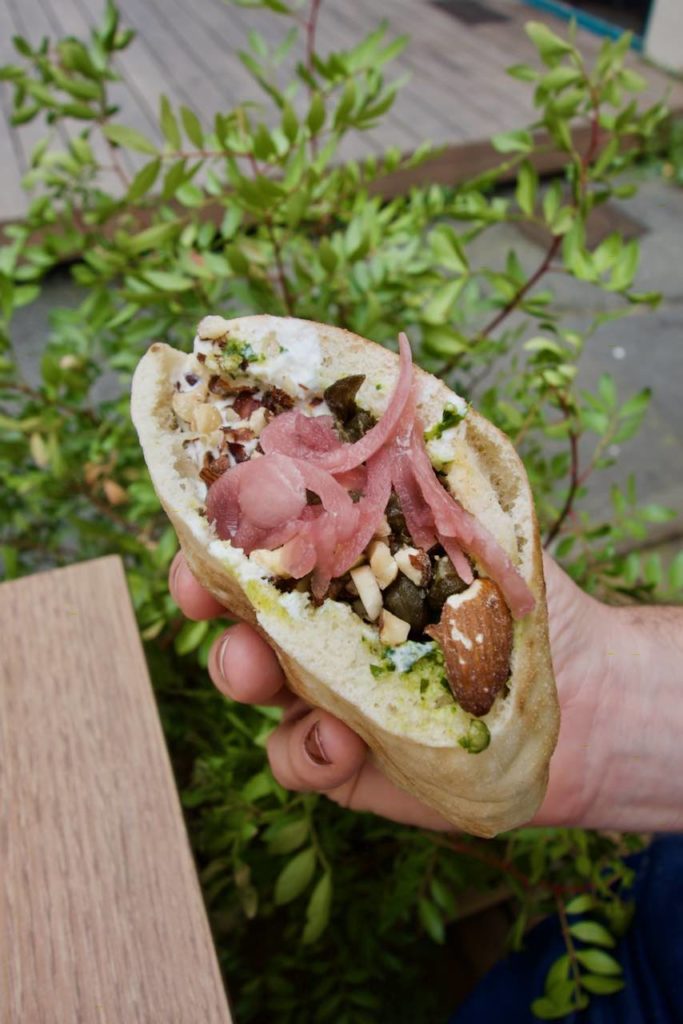 Pita aux amandes, pickles d'oignon, straciatella et herbes devant des plantes vertes