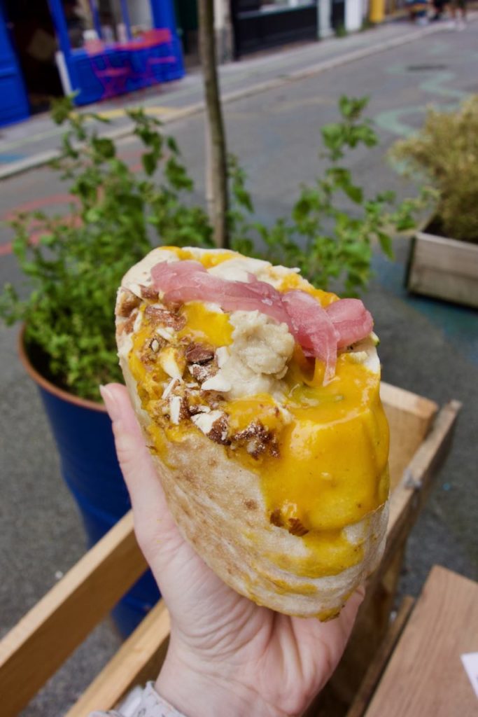 Pita avec sauce orange mangue, pickles roses et sauce tahini, des plantes vertes dans le fond