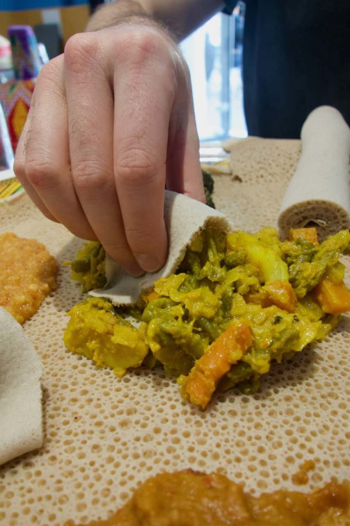 Gros plan sur la main d'une personne saisissant un wat avec un bout d'injera
