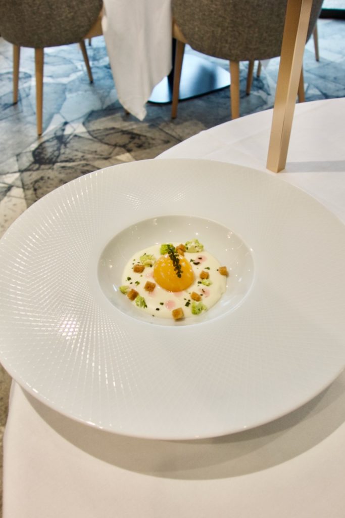 Oeuf en cuisson Hervé This au milieu d'un espuma de chou fleur blanc dans une grande assiette blanche et ronde