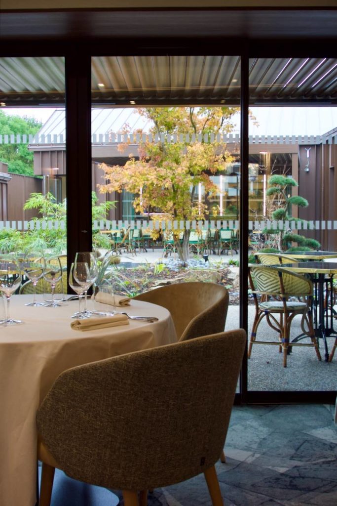 Vue de l'intérieur du restaurant, une table et des chaises à gauche et vue sur le patio depuis la baie vitrée