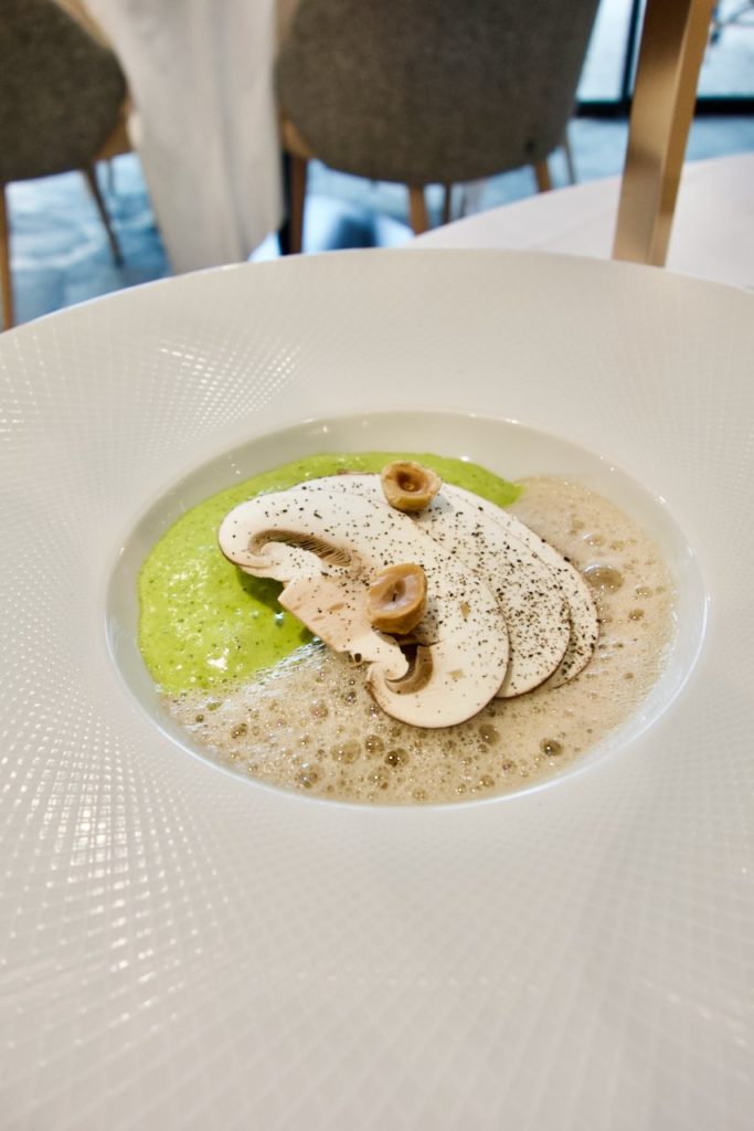 Carpaccio de champignon sur une persillade verte et une crème blanche dans une large assiette blanche