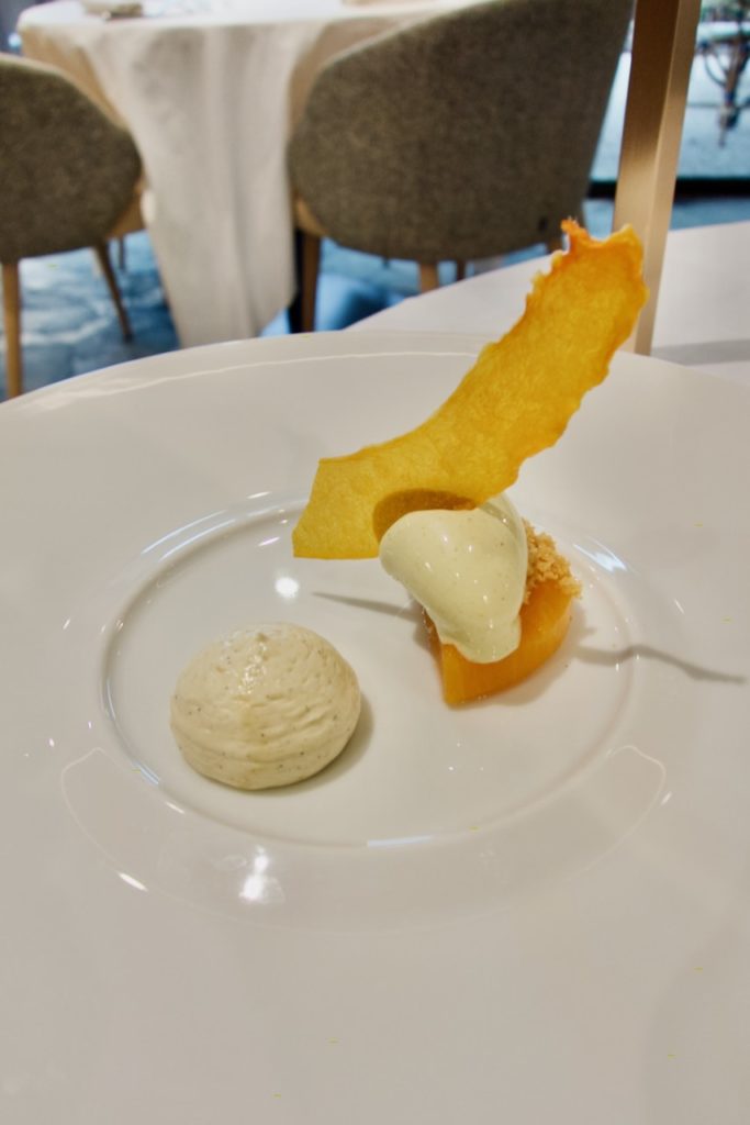 Demie courge surmontée de sablé breton, d'une crème glacé et d'une chips de courge, crème diplomate dans une large assiette blanche