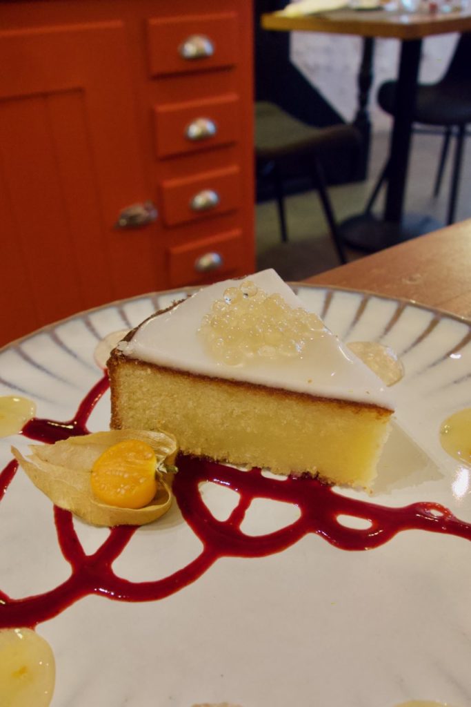 Part de gâteau nantais surmonté de perles de miel et accompagnée de coulis de fruits rouges et marmelade d'orange