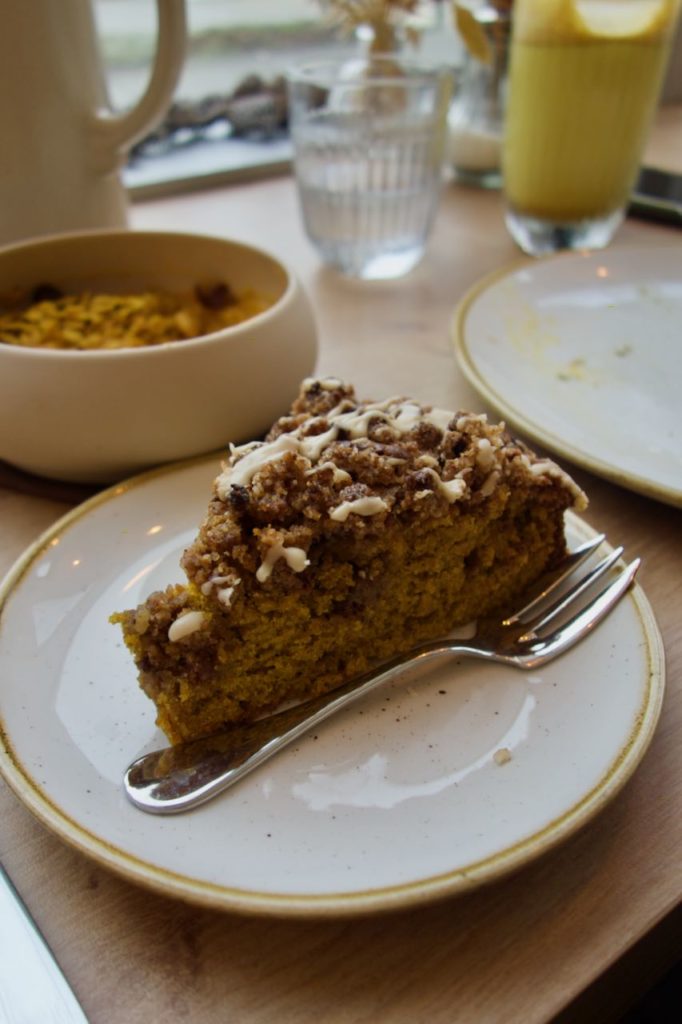 Part de gâteau avec une fourchette à trois dents dans une assiette en grès blanc et à liseré doré