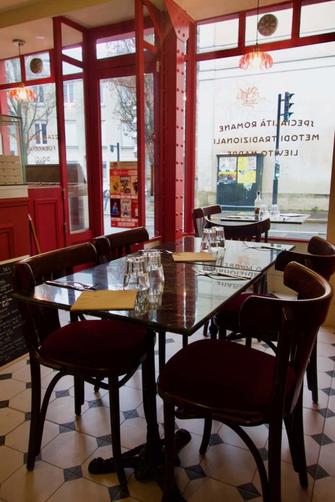 Intérieur du restaurant avec tables en bois, carrelage noir et blanc et zinc rouge